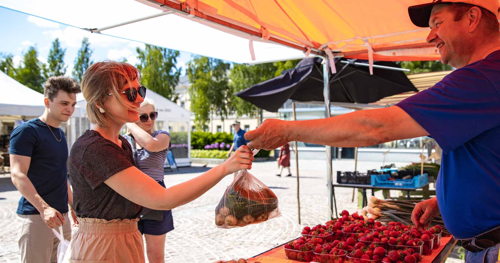 Torikauppias ojentaa mansikkarasian nuorelle naiselle Mikkelin torilla. 