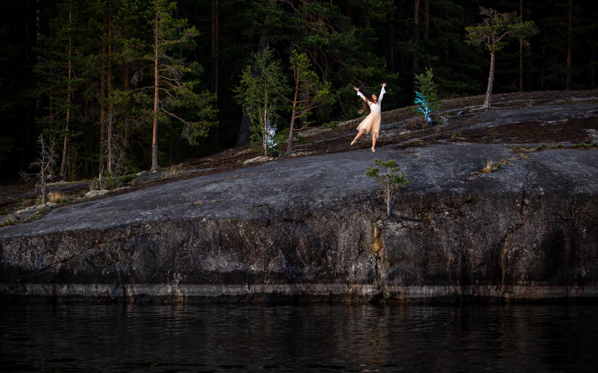 A woman dancing on a rock by a lake. 