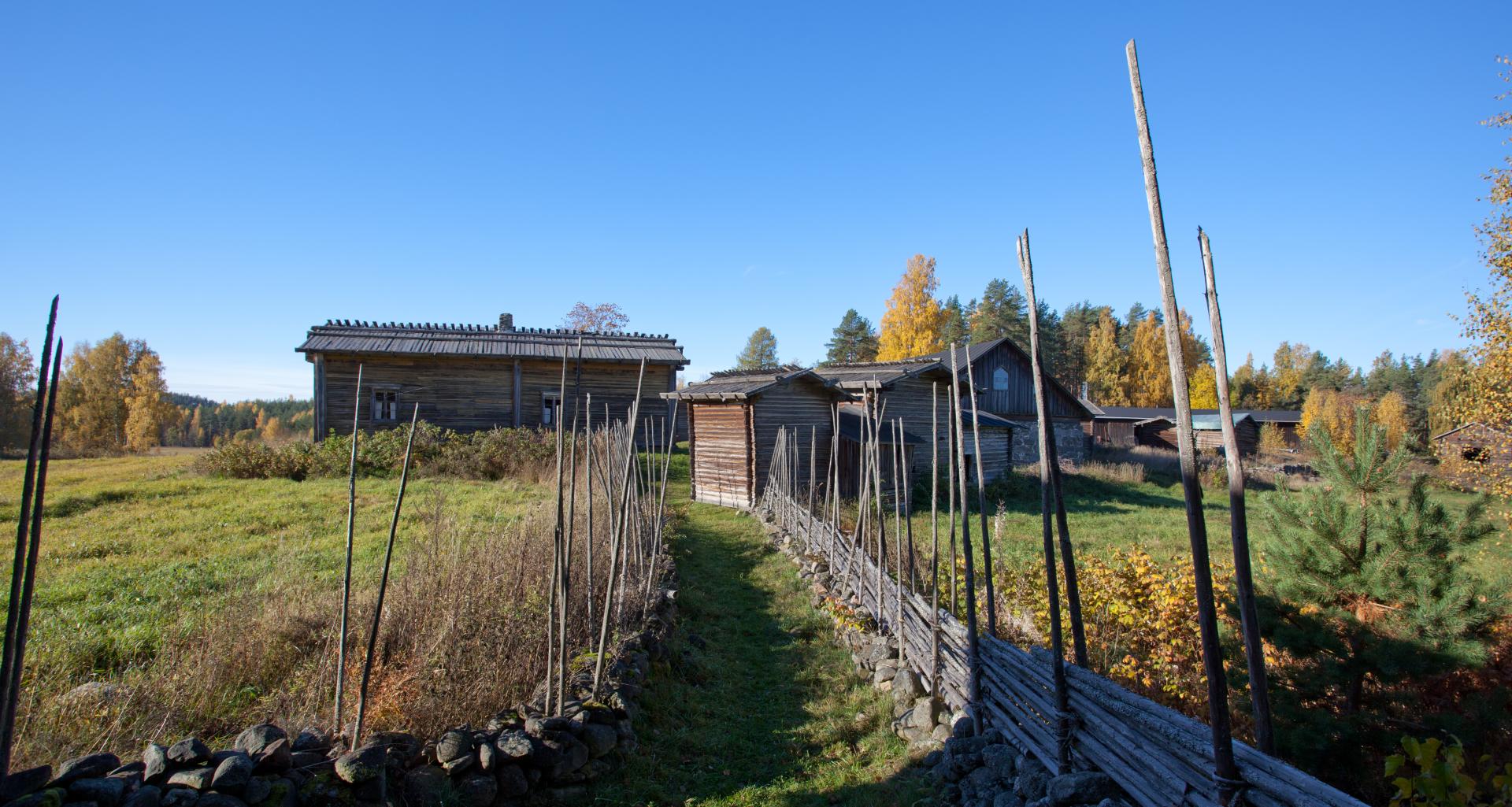 Ein Weg führt zu einem Hof, der von alten Holzhäusern und Hütten gesäumt ist. 