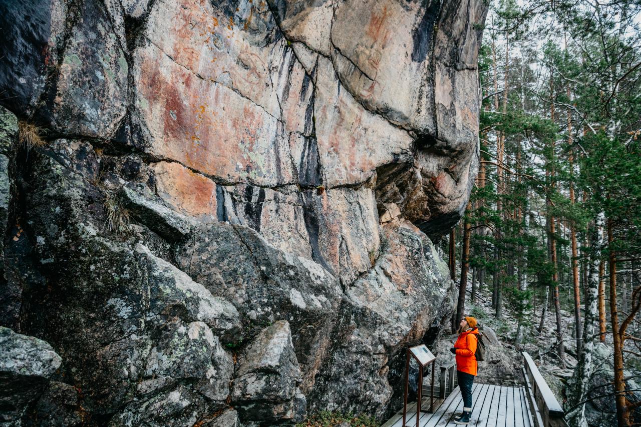 Nainen katselee kalliomaalauksia kallion juurella. 