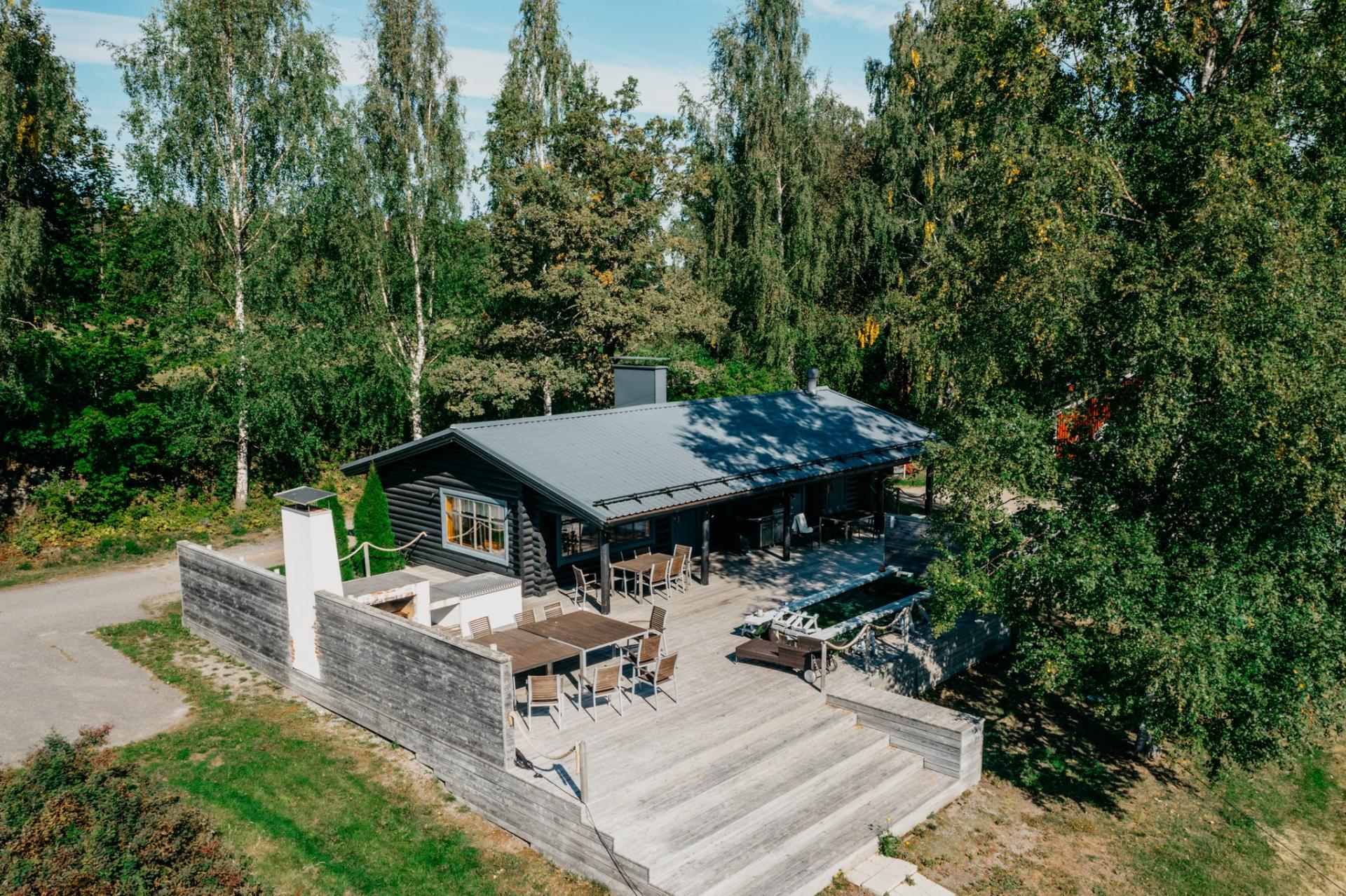 A modern sauna building with a large deck and seating groups by a lake. 