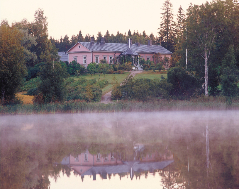 An old manor house and garden in the morning mist by a lake.