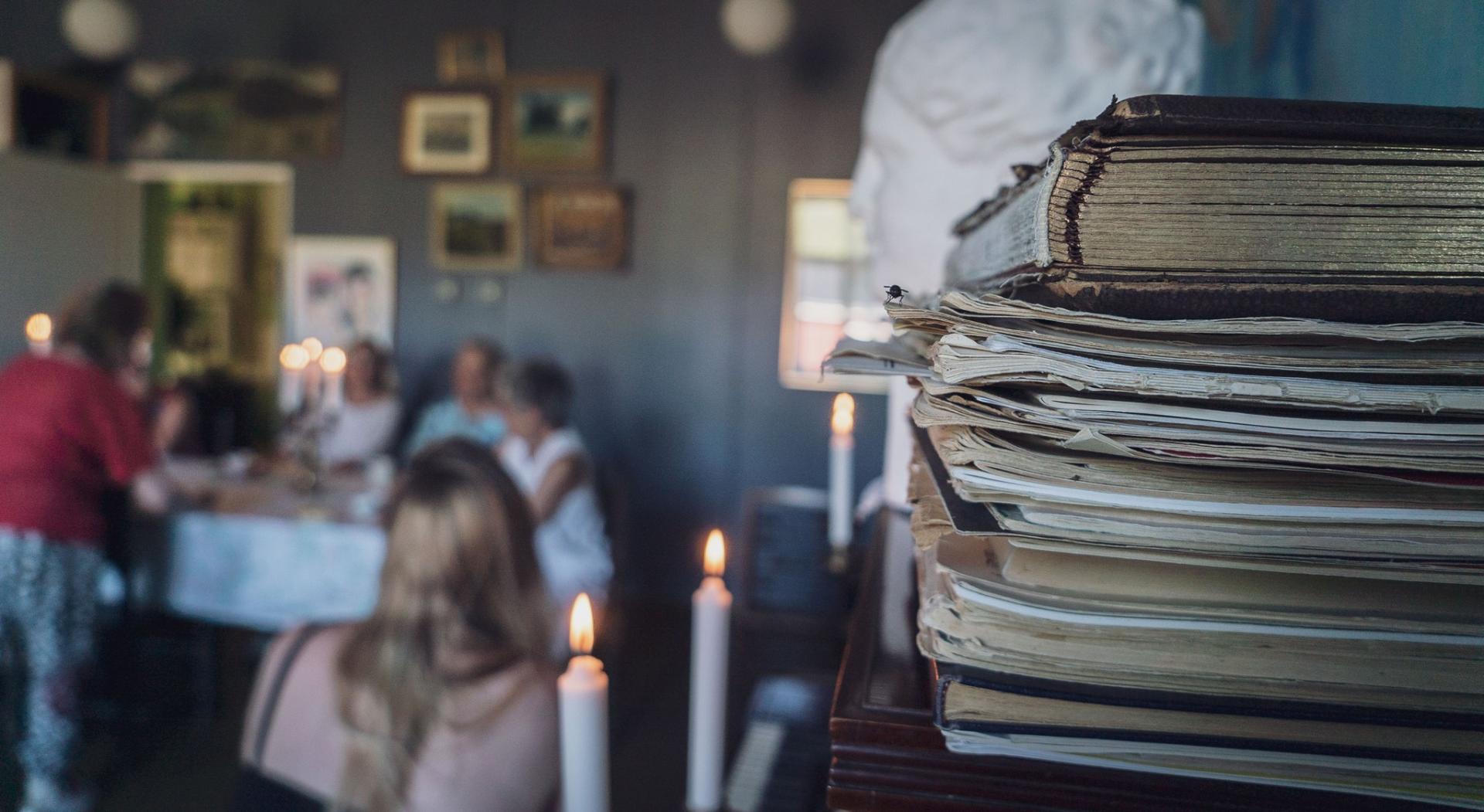 A pile of music books, lit candles and, in the background, women around a table.