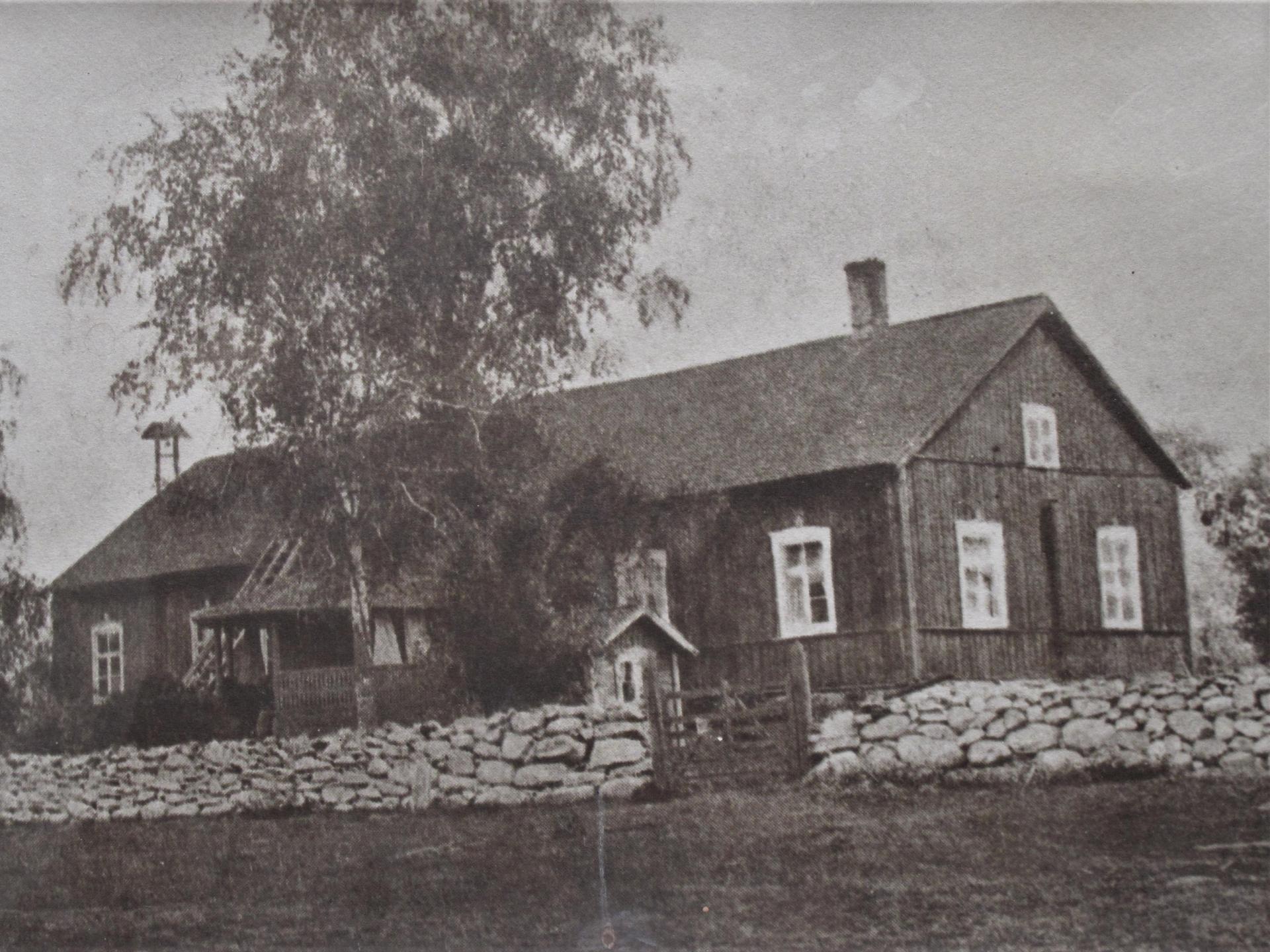 Old wooden building with a porch and a stone wall in front of the house. 