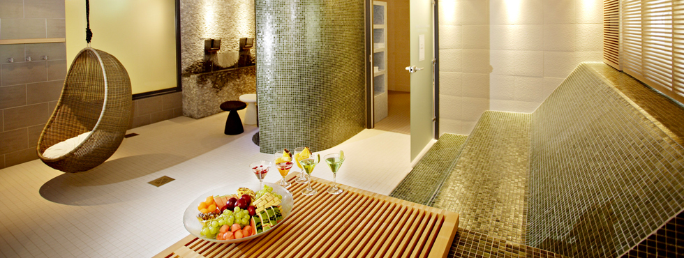 Kylpylän huone, jossa on korituoli, muotoiltu kaakelipenkki ja pöydällä hedelmiä ja juomia. 