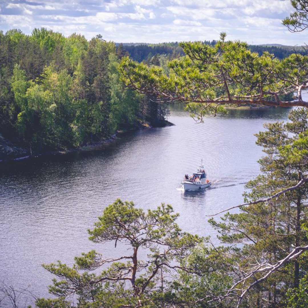 A boat in a strait on both side of which are high rock cliffs with trees. 