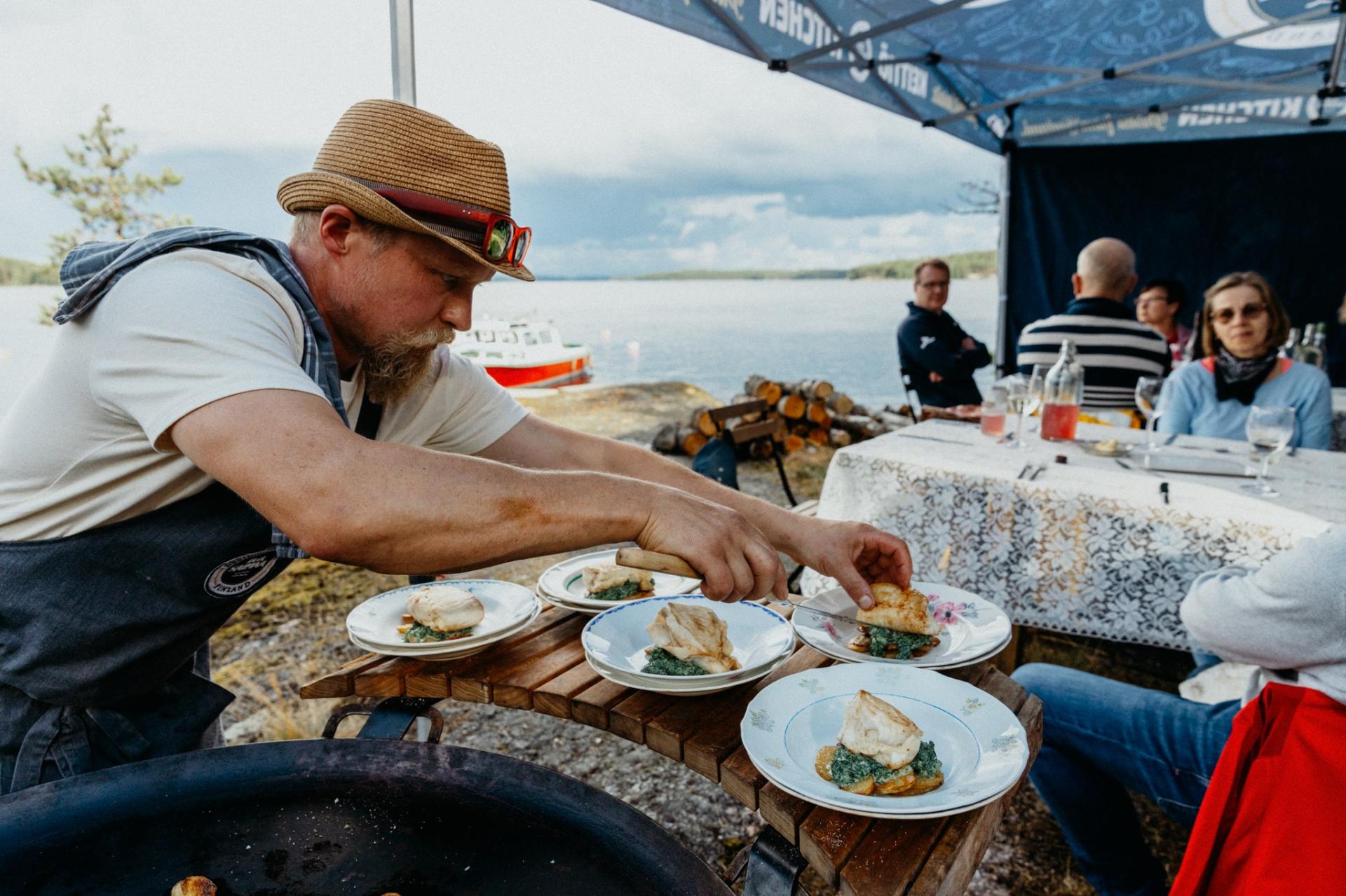 A man is preparing dishes on plates outdoors by a lake. 