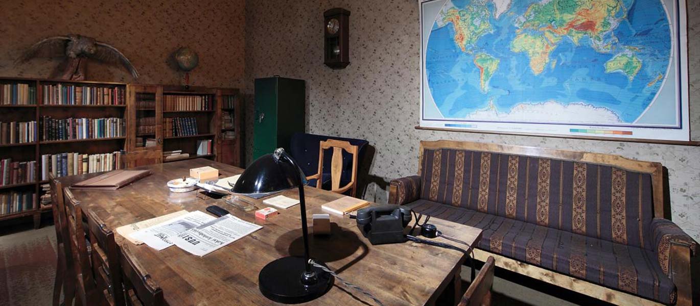 Mannerheimin työhuone, jossa on vanha puinen kirjoituspöytä, lankapuhelin, pöytälamppu, kirjahylly, sohva ja seinällä maailmankartta. 