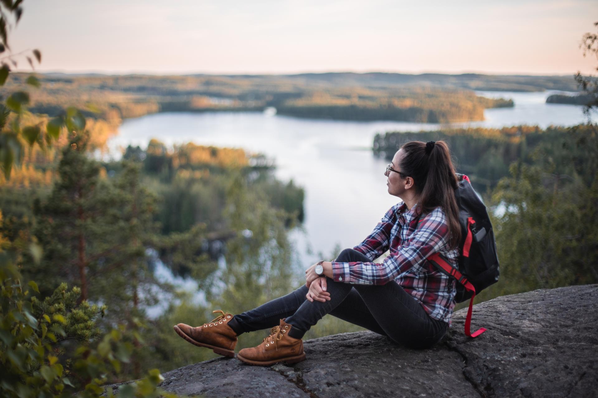 Eine Frau sitzt auf einem Felsen und blickt auf die Landschaft. 