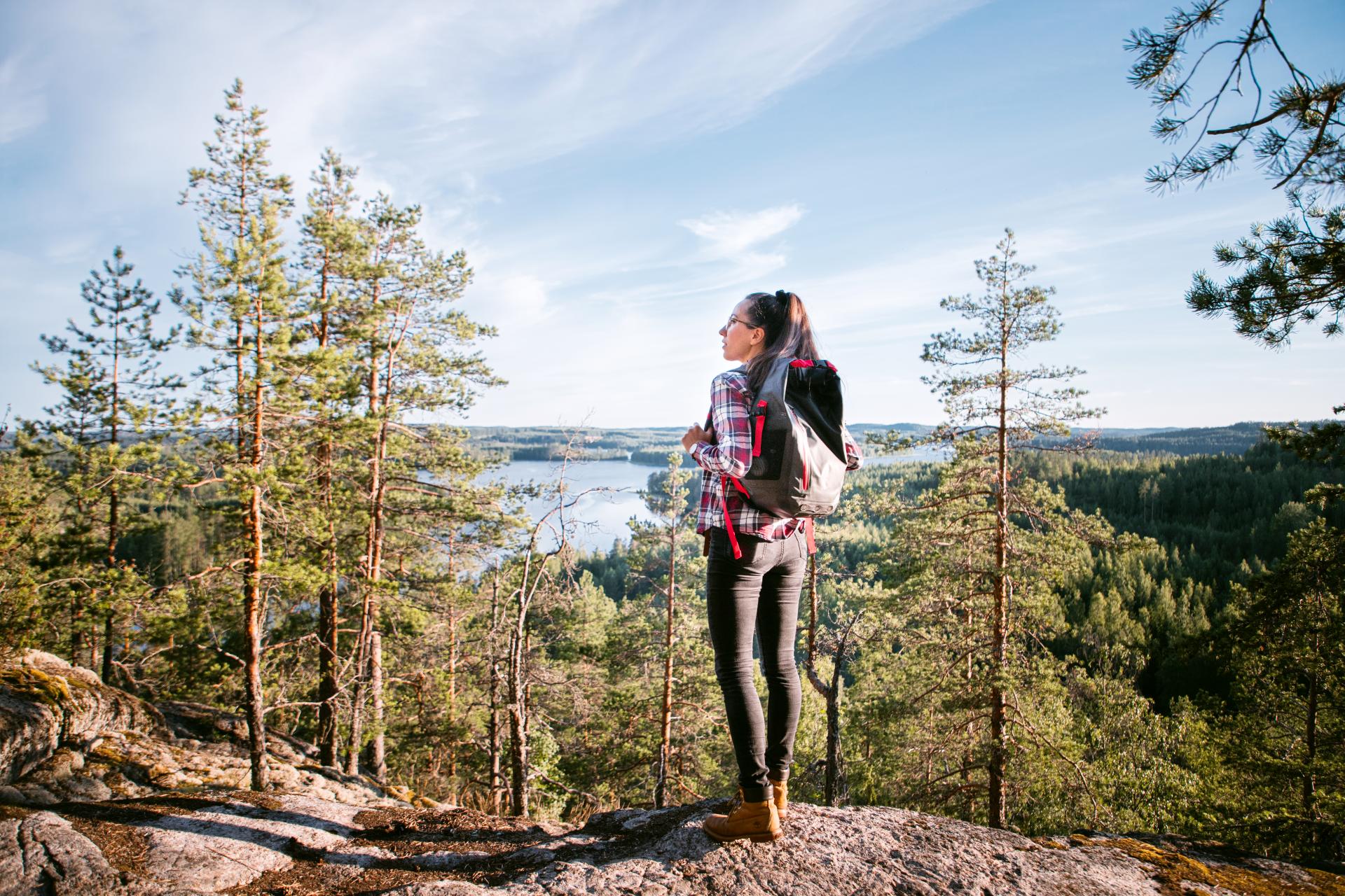 A woman with a backpack stands at the top of the Neitvuori hill and looks out over the landscape. 