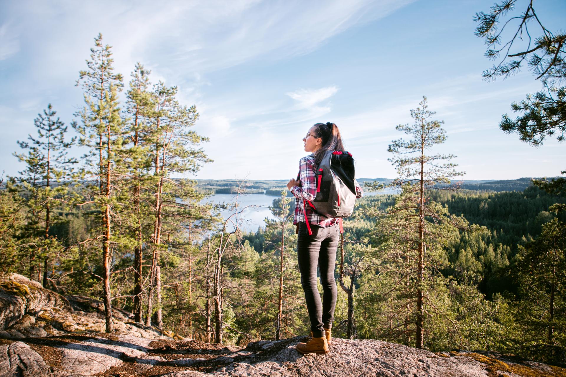 Nainen reppu selässä seisoo Neitvuoren kallion laella ja katselee maisemia. 