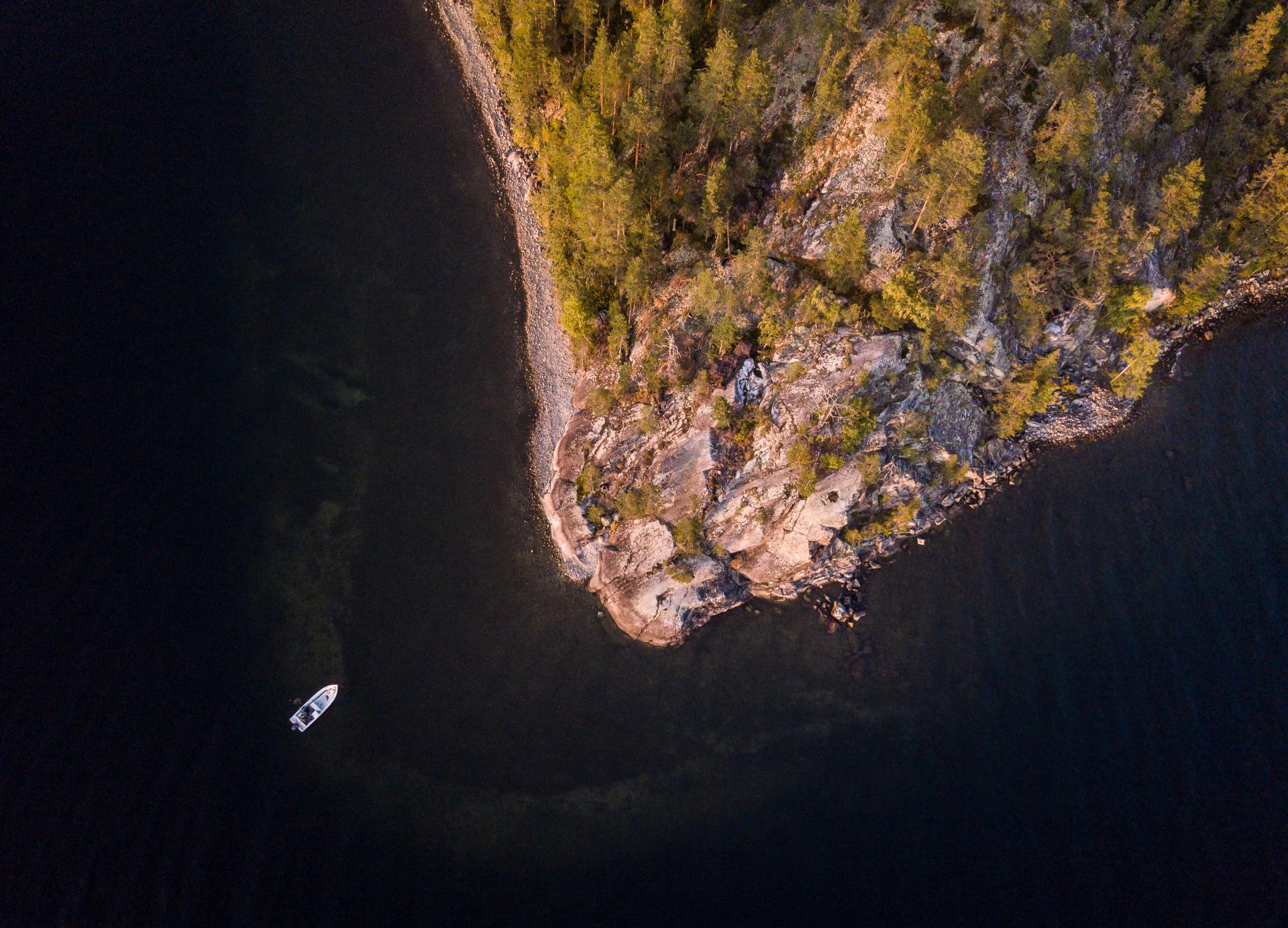 Eine felsige Landzunge von oben gesehen und ein Boot vor dem Felsen. 