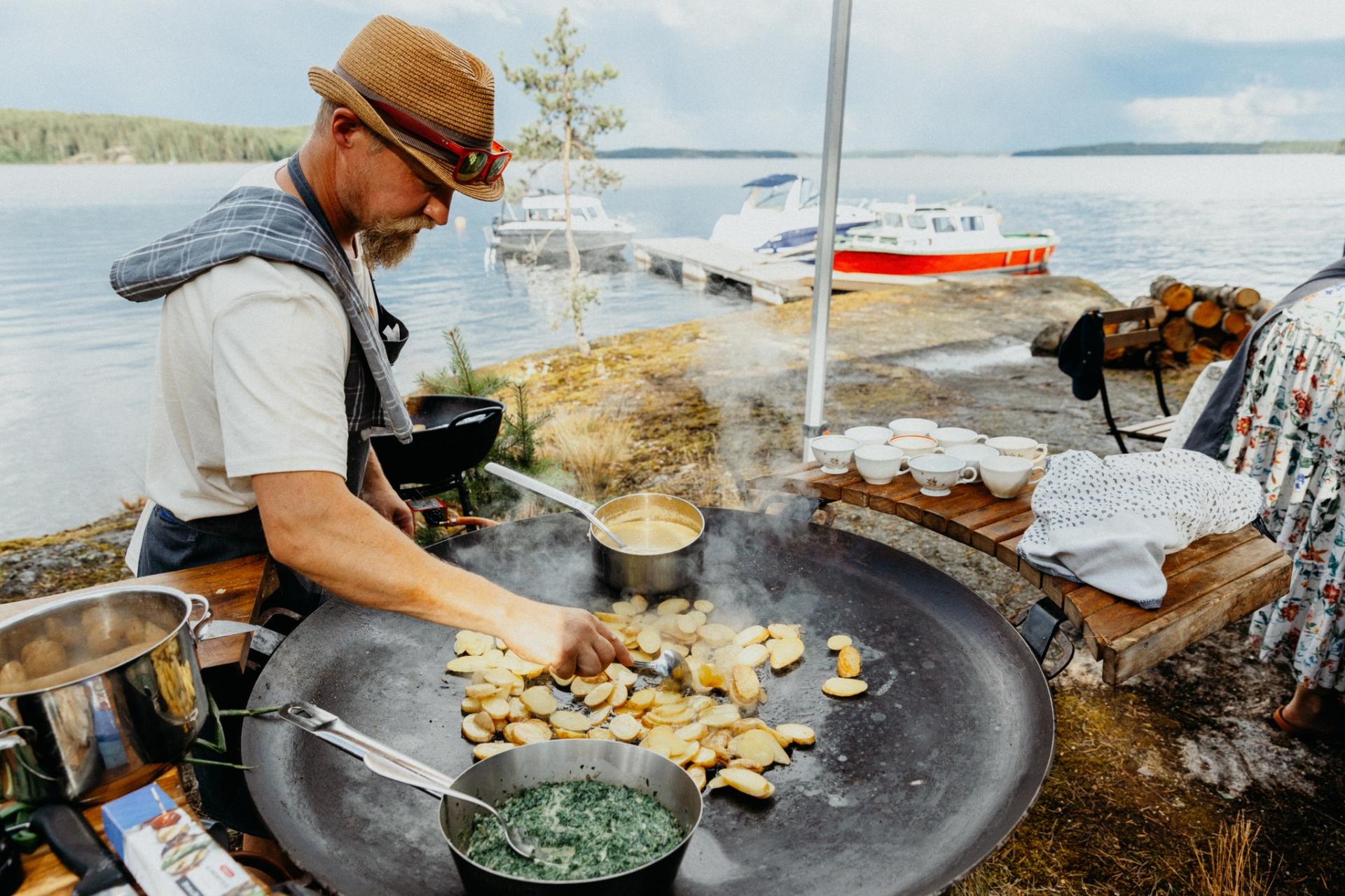A man is preparing food on a large frying pan on a shore of an island . 