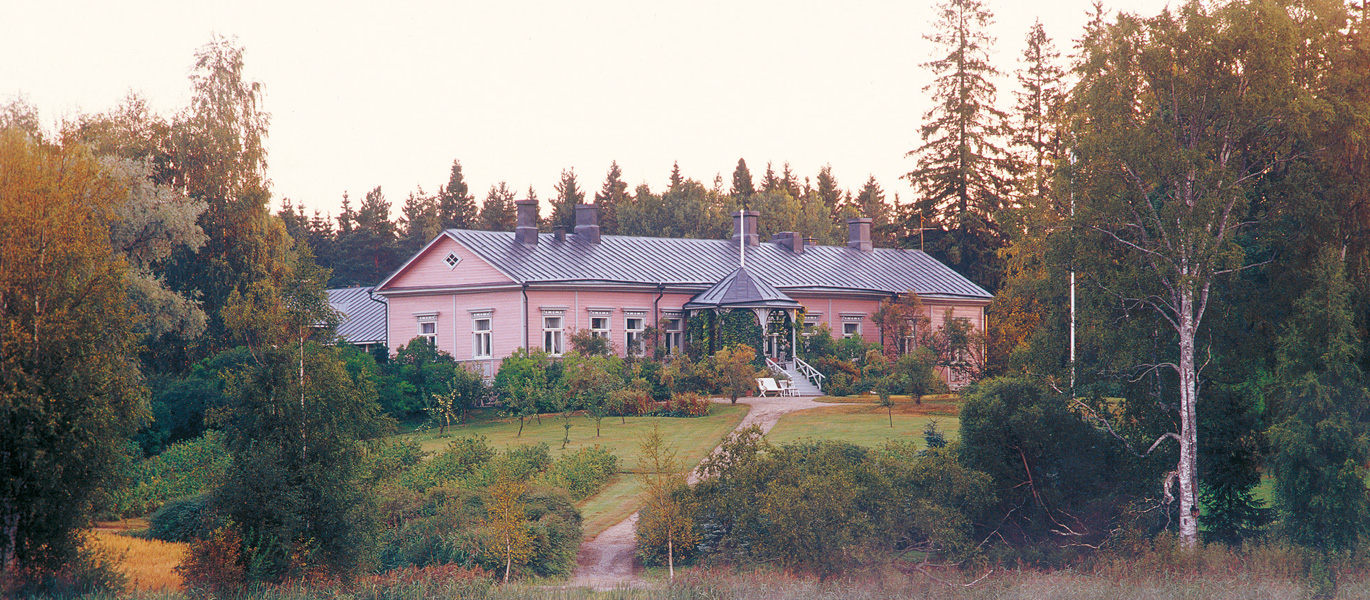 Kaunis vanha puinen kartanorakennus vehreän puutarhan keskellä.